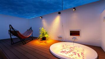 Un baño exterior moderno con jacuzzi, una hamaca y una planta en maceta.