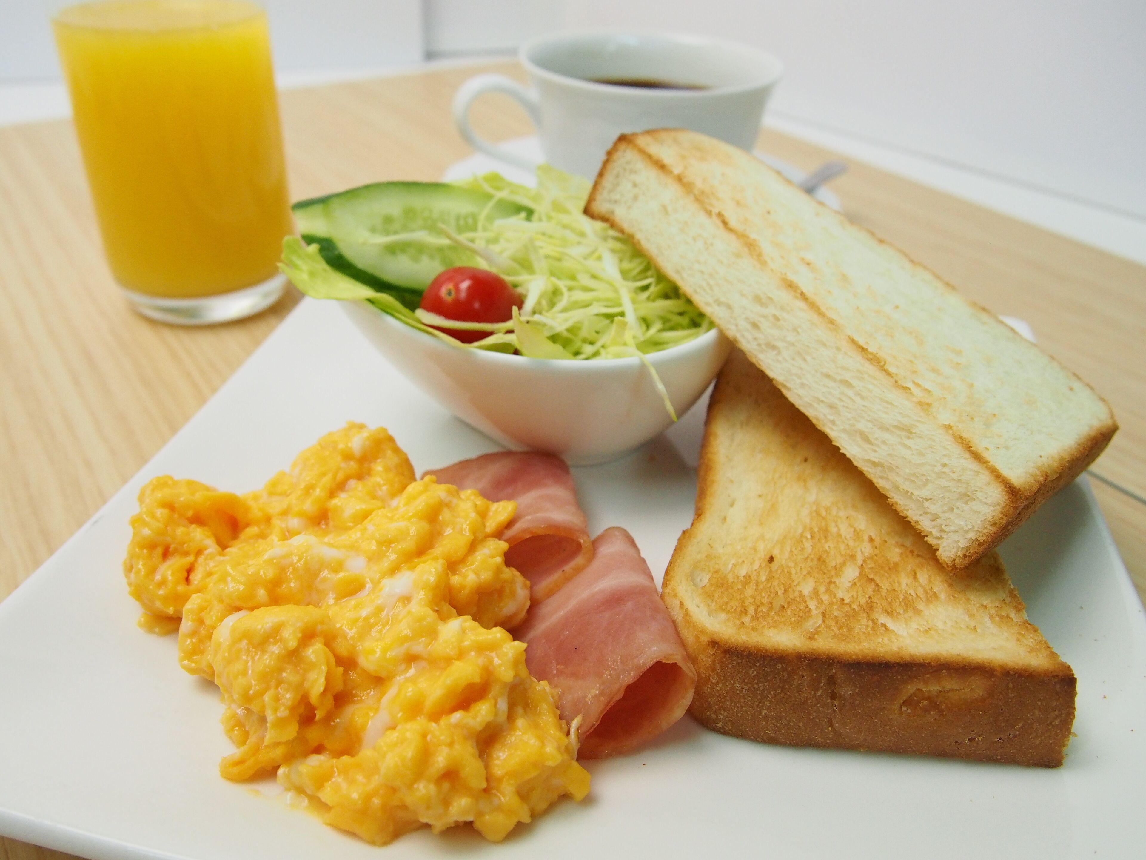A breakfast plate with scrambled eggs, ham, toast, a salad, and a glass of orange juice.