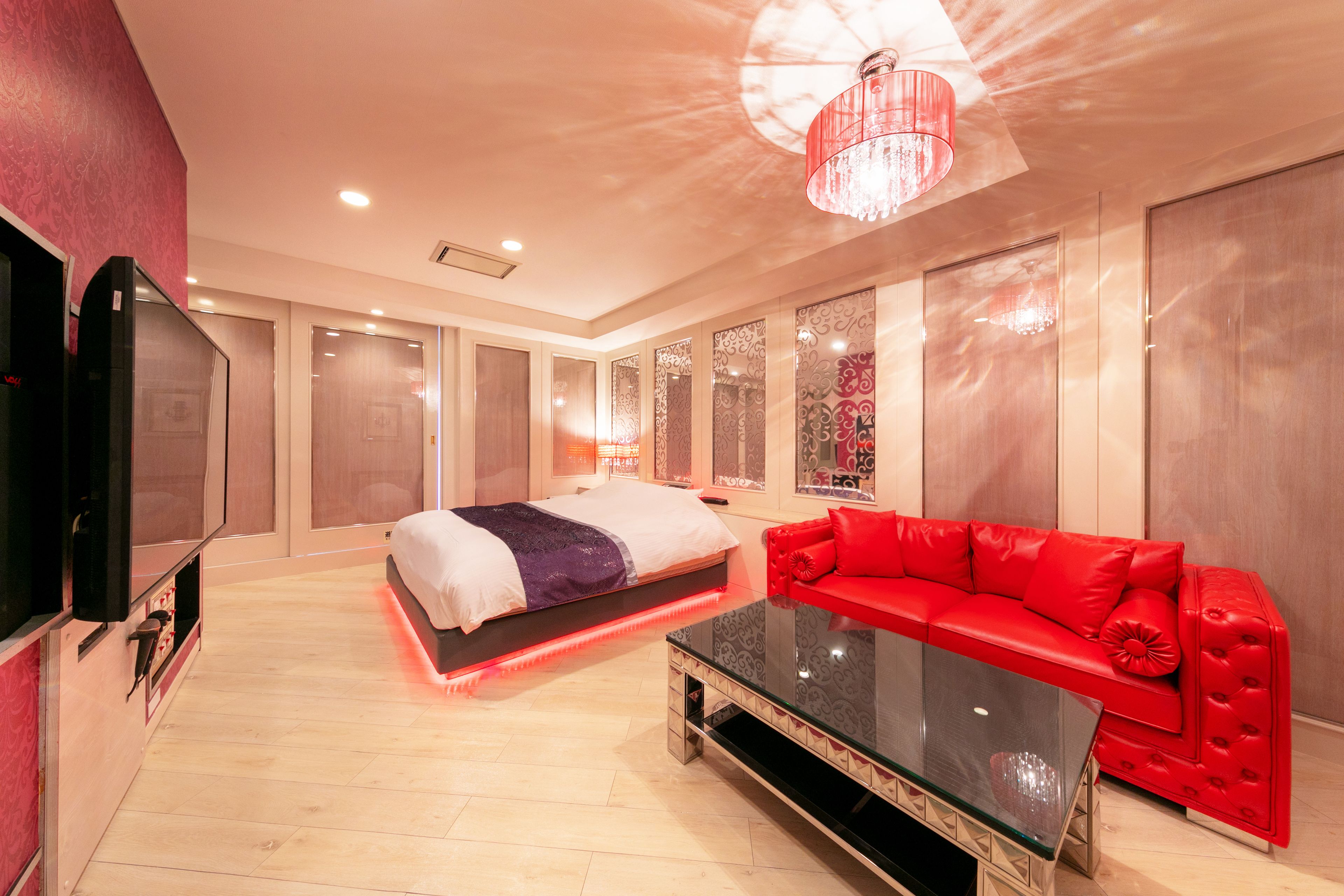 A modern hotel room with a bed, a red sofa, a glass coffee table, and a TV.
