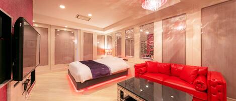 A modern hotel room with a bed, a red sofa, a glass coffee table, and a TV.