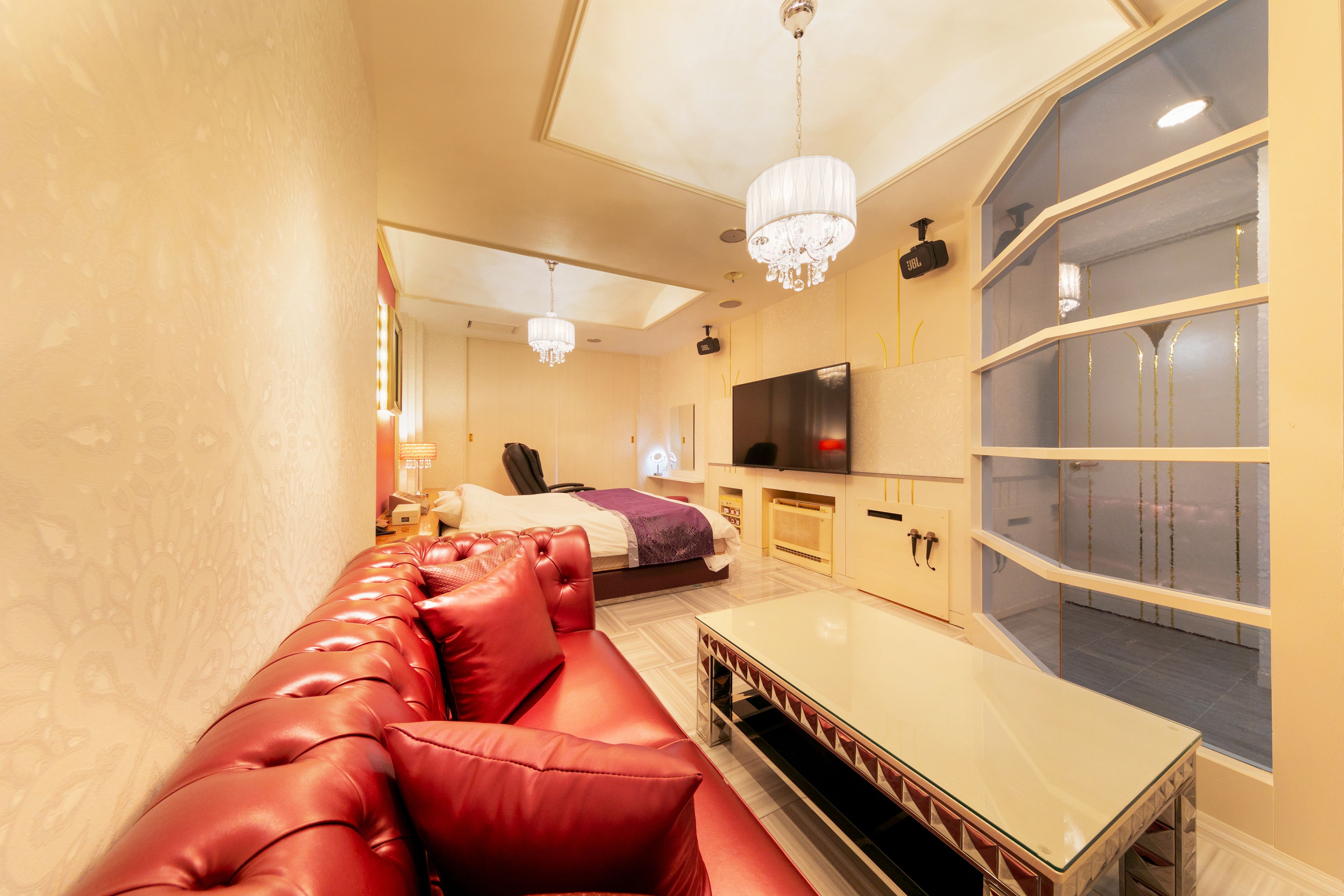 Una sala de estar moderna con un sofá de cuero rojo, una mesa de centro de vidrio y un televisor grande en la pared.
