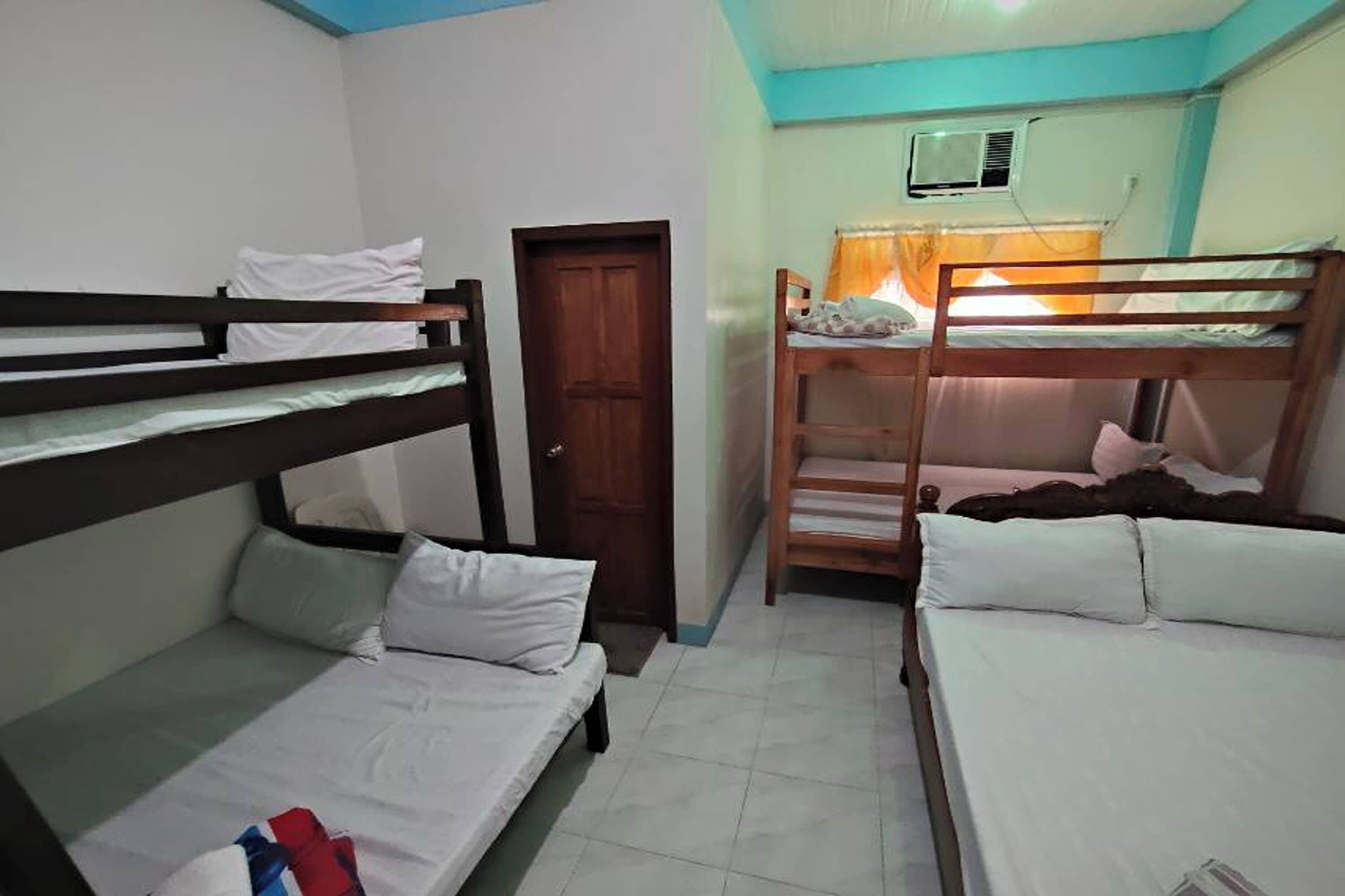A dormitory room with bunk beds, a door, and an air conditioning unit.
