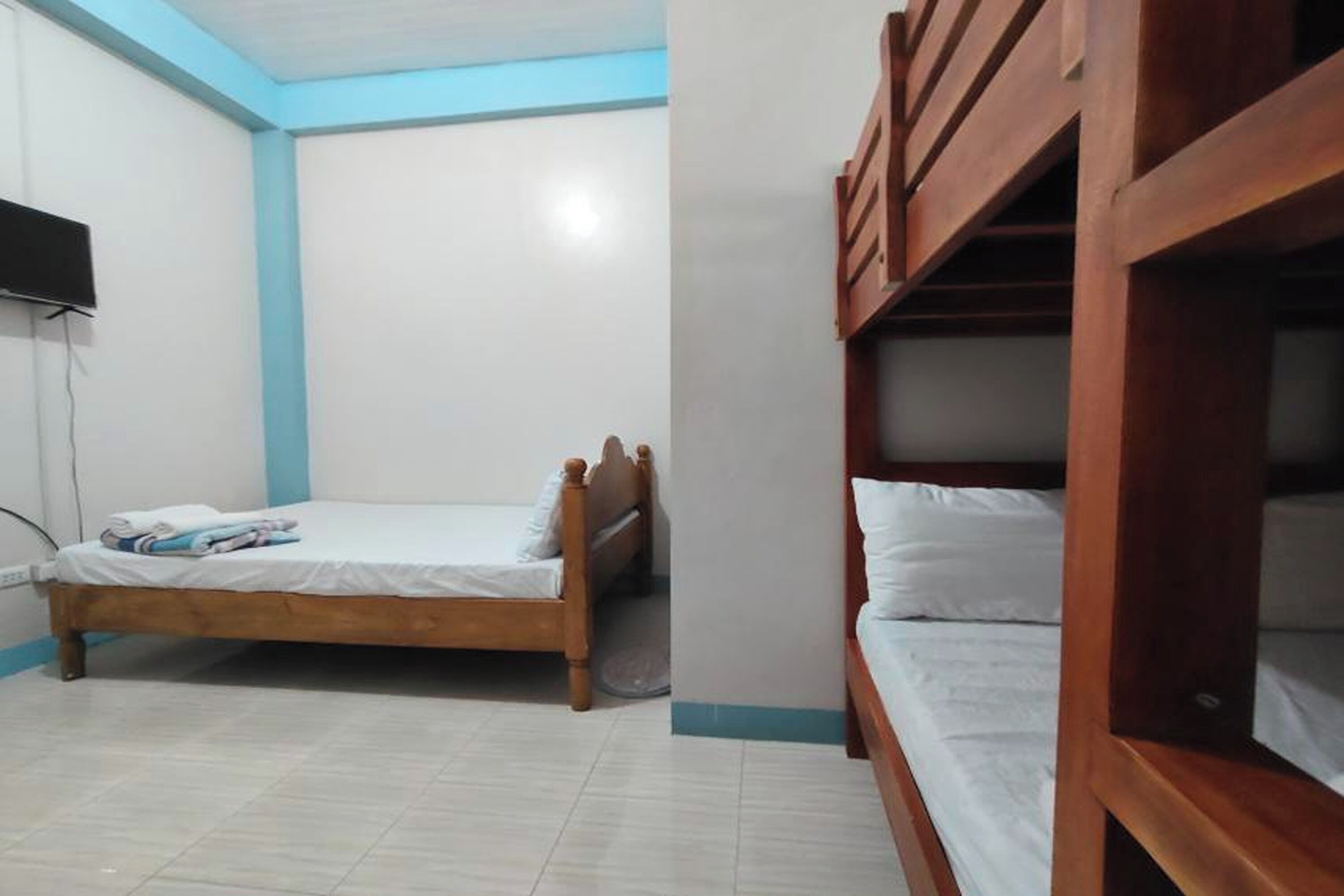 Una habitación con una cama individual, un televisor en la pared y una cama alta en una esquina.