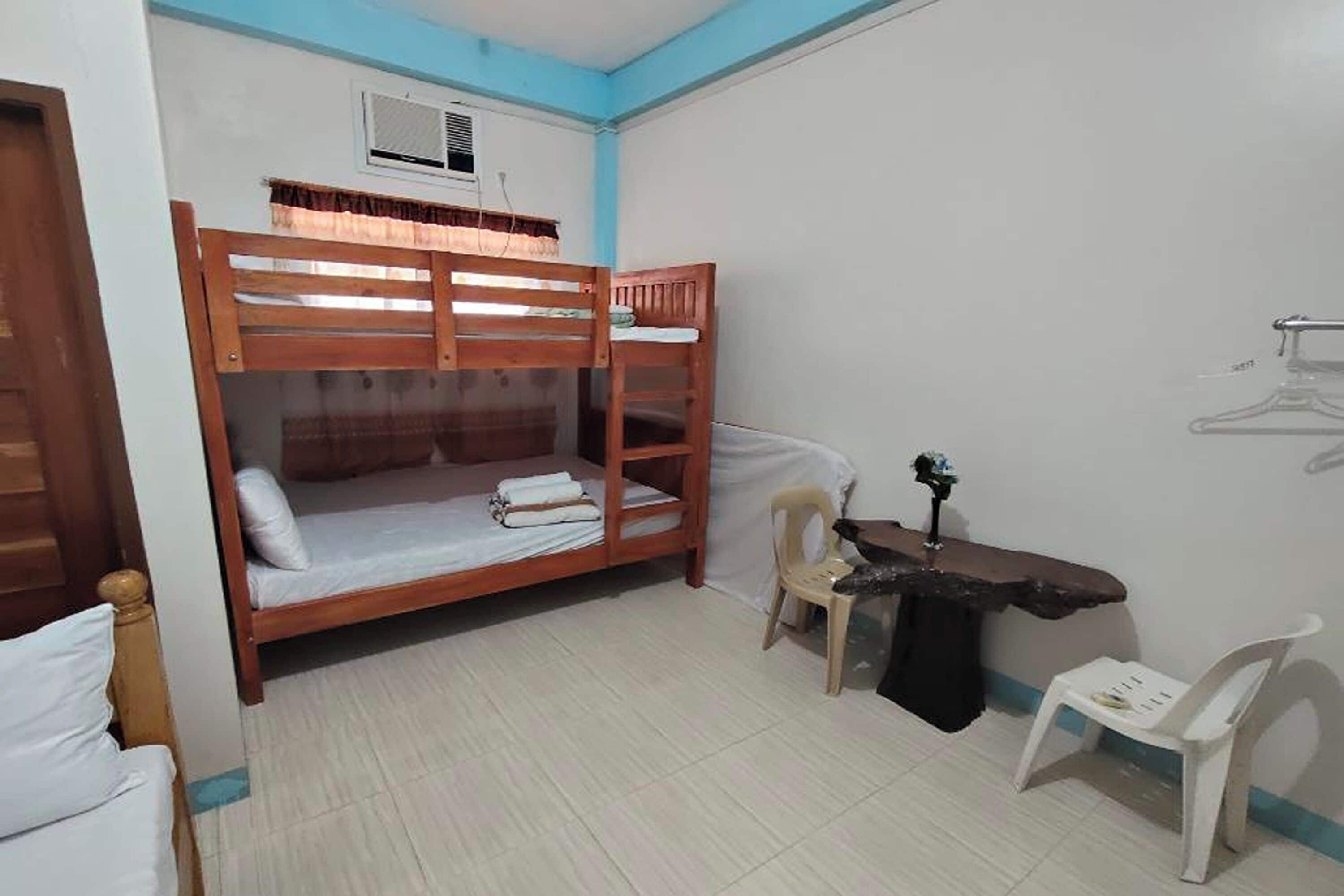 A dormitory room with bunk beds, a desk, a chair, and a radiator.