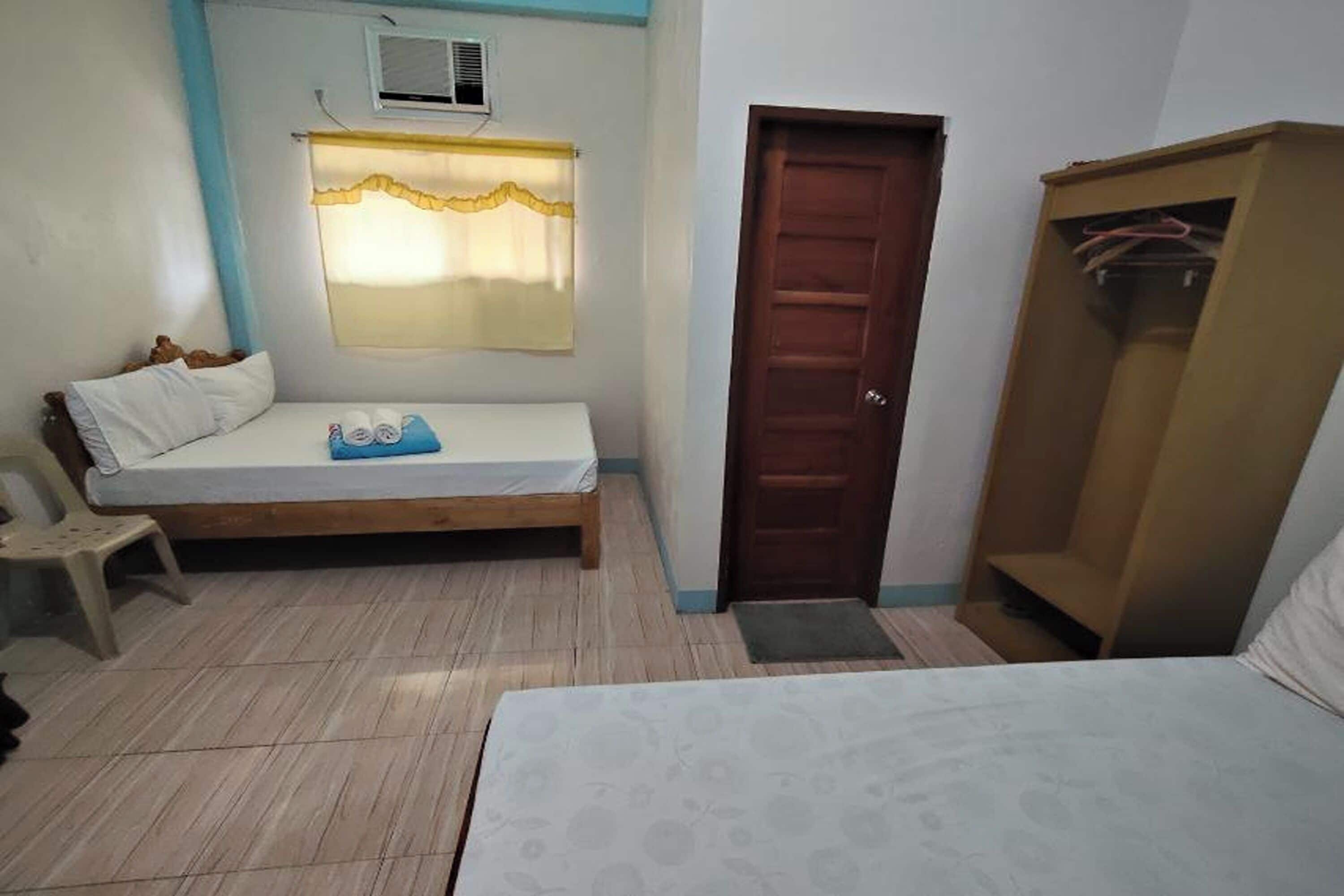 Una habitación pequeña y sencilla con una cama individual, un armario de madera, una silla pequeña y una puerta.