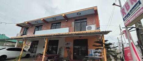 A two-story building with a flat roof, a covered front porch, and a signboard advertising a restaurant.