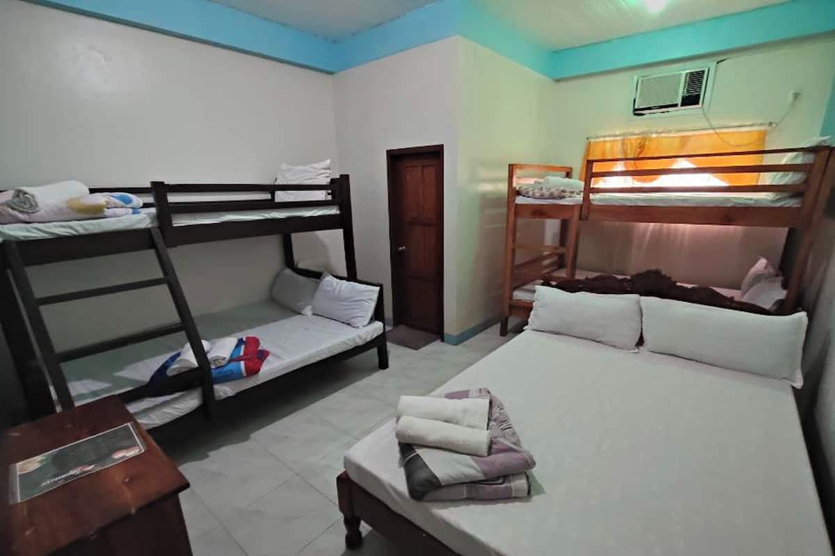 A dormitory room with bunk beds, a wooden desk, and a door.