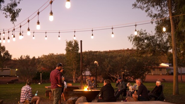 A group of people gathered around a campfire in an outdoor setting with string lights overhead. - Cheela Plains Station (Nanutarra)
