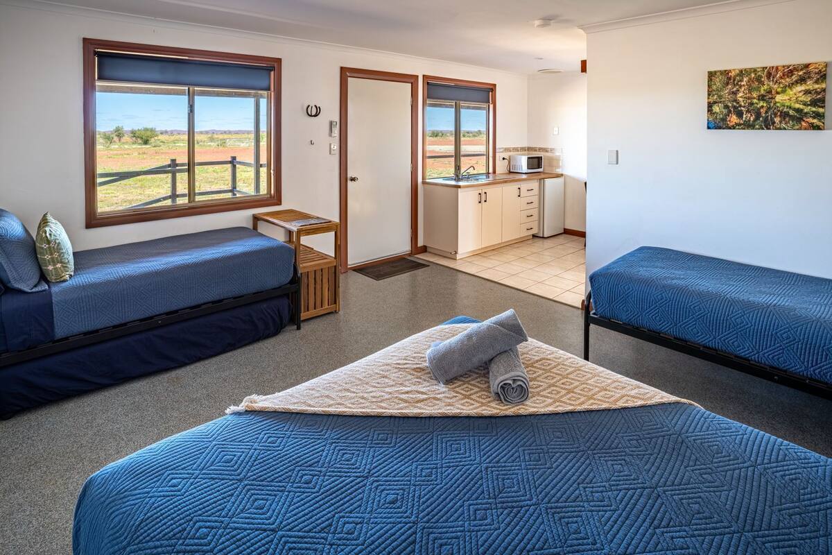 A compact room with two beds, a small kitchenette, and a view of the outdoors.