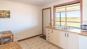 A compact kitchen with a wooden countertop, a sink, and a window with a view of a grassy landscape. - Cheela Plains Station (Nanutarra)