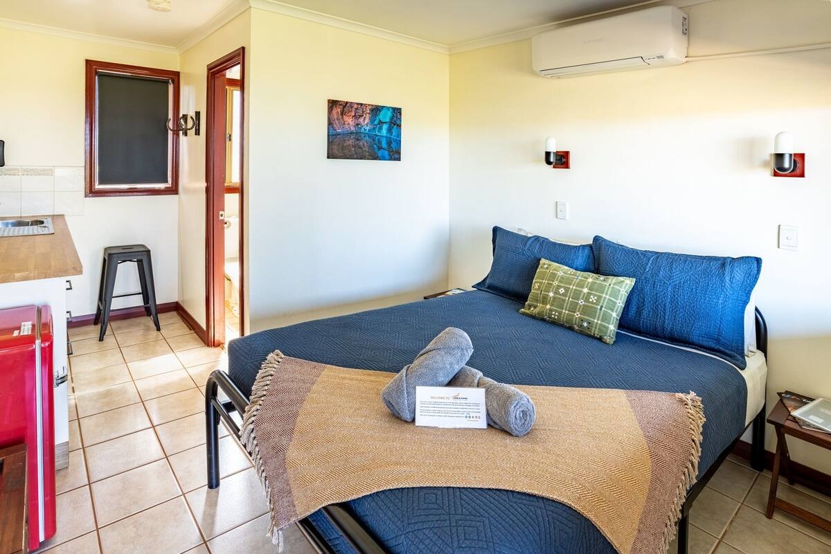 A bedroom with a bed, a desk, a chair, and an air conditioning unit.