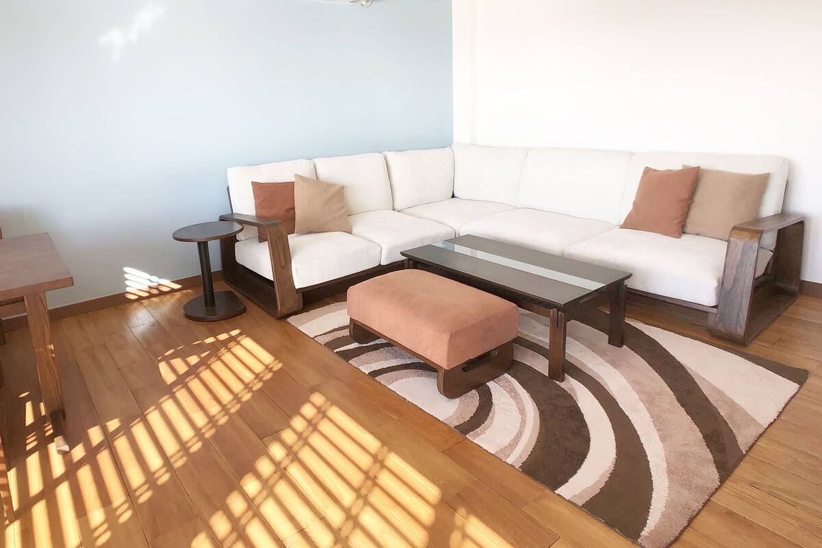A modern living room with a white sofa, a round coffee table, a wooden side table, and a striped rug.