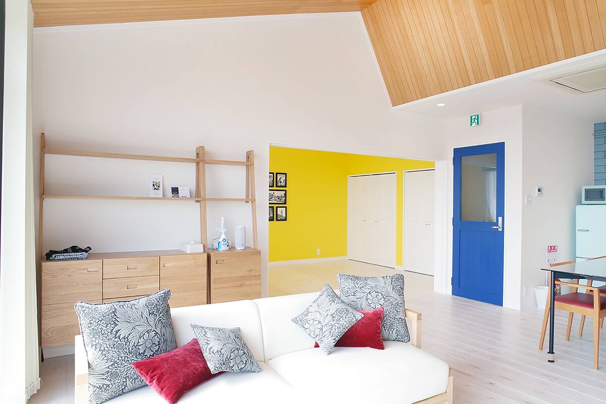 A modern living room with a white sofa, wooden shelves, and a bright yellow accent wall.