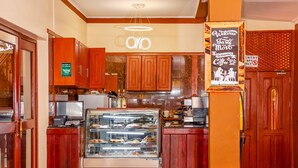 A bakery counter with a glass display case, wooden cabinets, and a sign advertising coffee. - New Safari Hotel (Arusha)