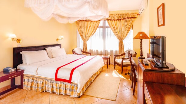 A hotel room with a large bed, a desk with a television, and a chair. - New Safari Hotel (Arusha)