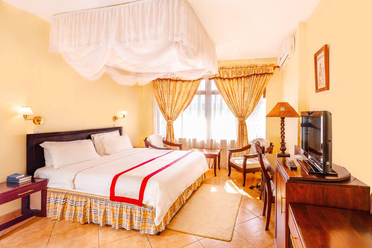 A hotel room with a large bed, a desk with a television, and a chair.