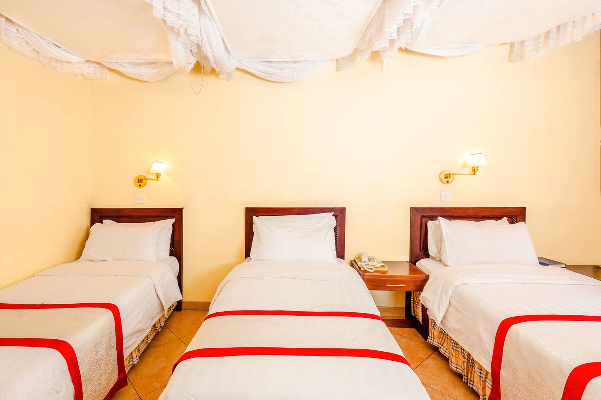A hotel room with two single beds, each with a wooden headboard, white bedding, and a red trim. There are bedside tables with lamps and a telephone.
