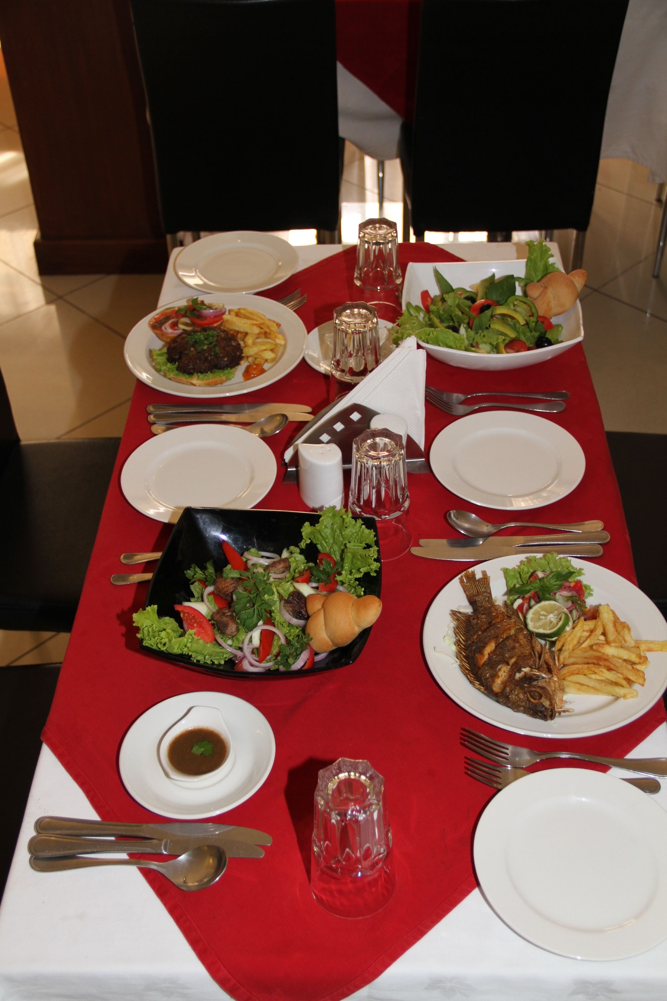 A dining table set with various dishes, including salads, fish, and fries, along with cutlery and glasses.