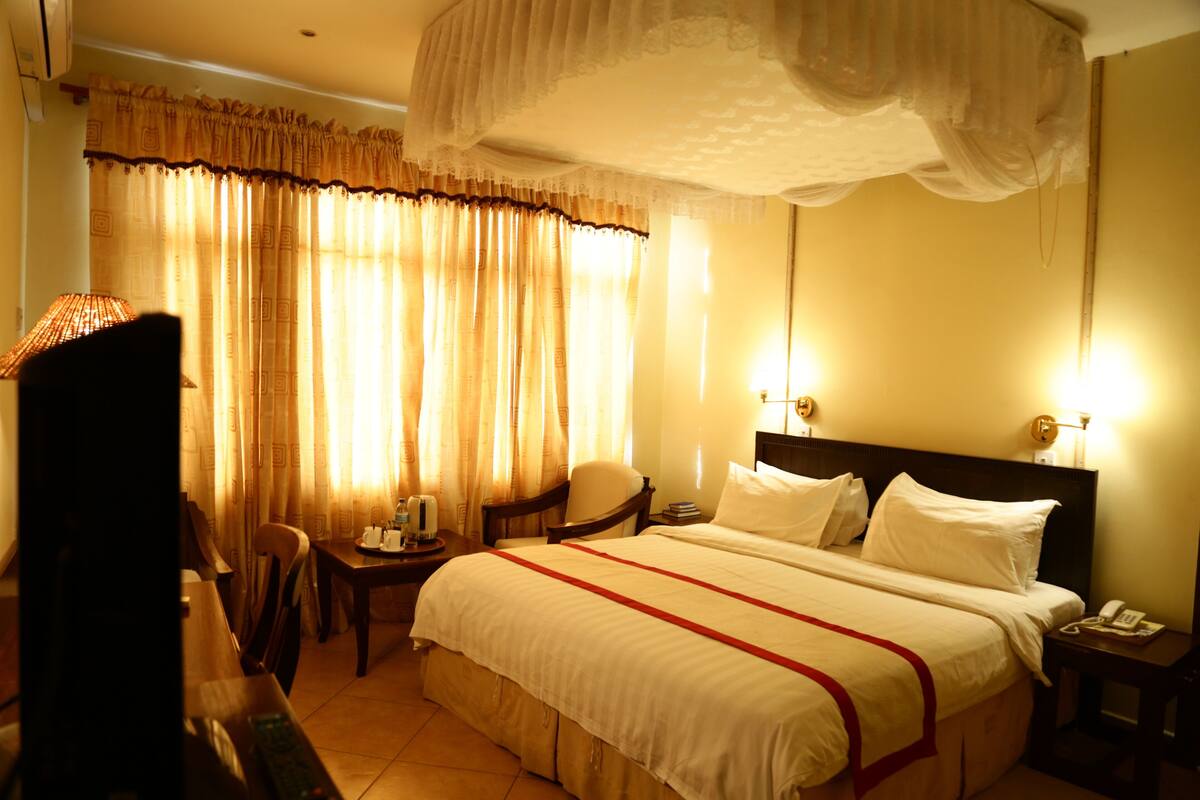 A hotel room with a large bed, a chair, a small table, and a nightstand with a phone.