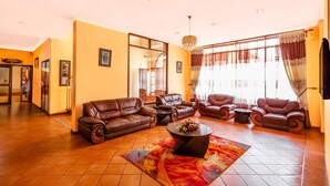 A spacious living room with leather sofas, a coffee table, and a large window with curtains. - New Safari Hotel (Arusha)