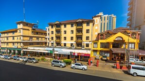 A street view with multiple buildings, including a yellow building with balconies and a pizzeria coffee bar. - New Safari Hotel (Arusha)