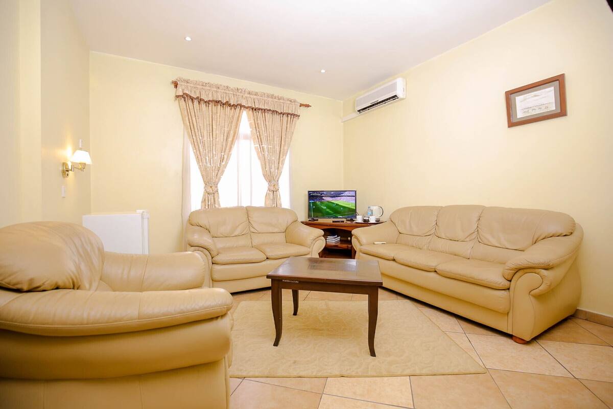 A living room with two beige leather sofas, a wooden coffee table, and a television on a stand.