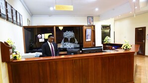 A reception desk with a wooden finish, a framed portrait above it, and a sign indicating the reception area. - New Safari Hotel (Arusha)