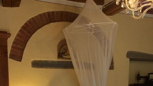 Een slaapkamer met een bed, nachtkastje, lamp, hemelbed en spiegel.