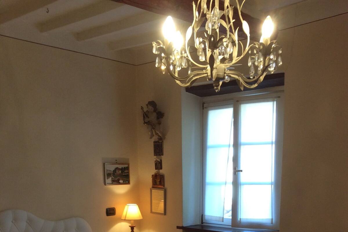 Ein Schlafzimmer mit einem Bett, einem Holzstuhl, einer Lampe, einem Fenster und einer Deckenleuchte.