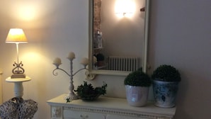 Een witte console tafel met een spiegel, twee planten in potten, een lamp en een decoratieve mand.