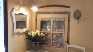 Een kleine kamer met een witte tafel, een witte stoel, een spiegel en een raam met kantgordijnen.