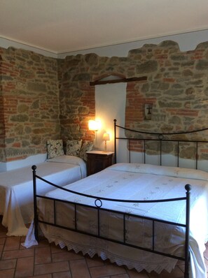 Une chambre avec un mur en pierre, un lit avec un cadre en métal et une table de chevet avec une lampe.