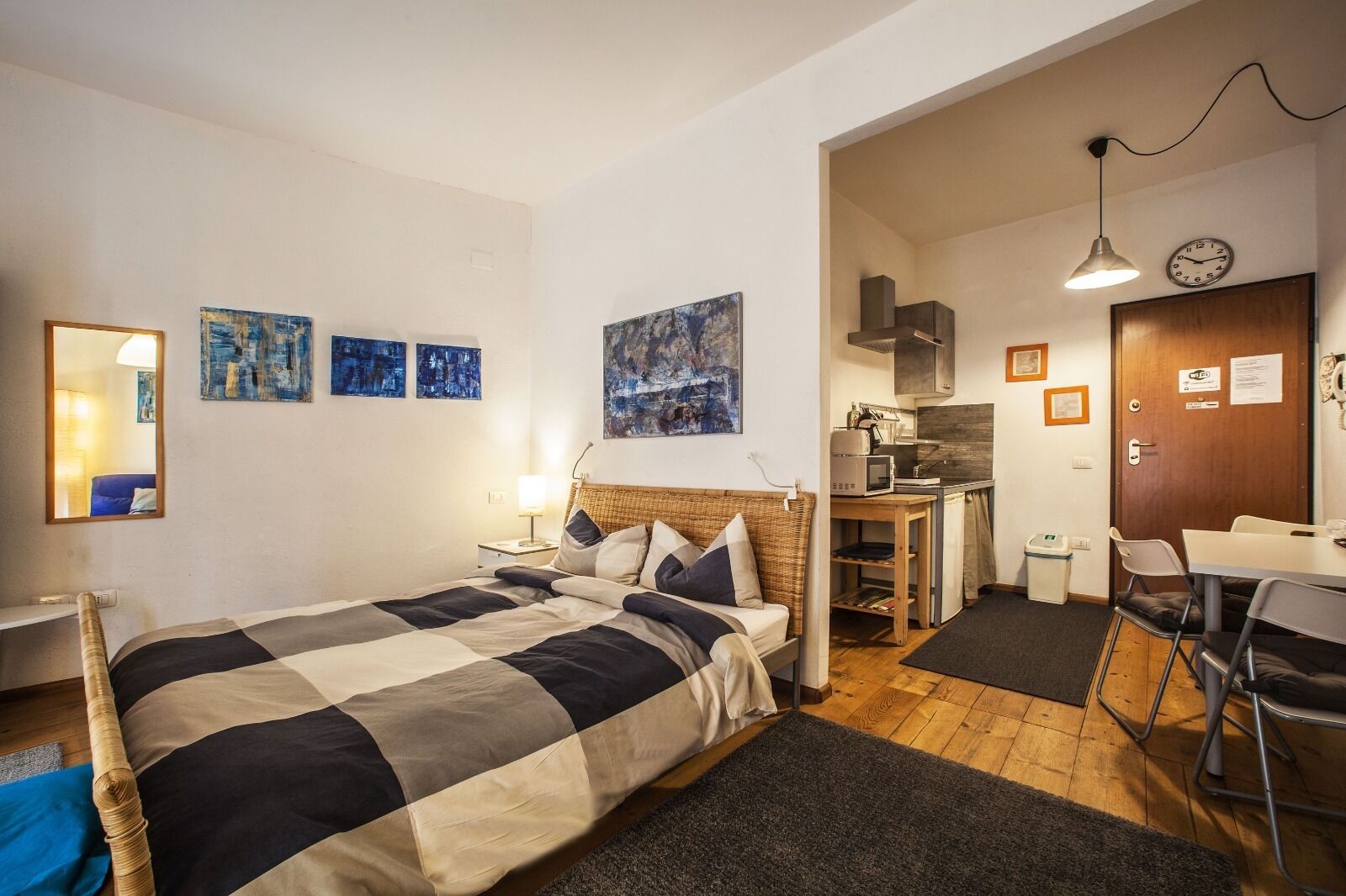 A compact hotel room with a bed, bedside table, lamp, and artwork on the walls.