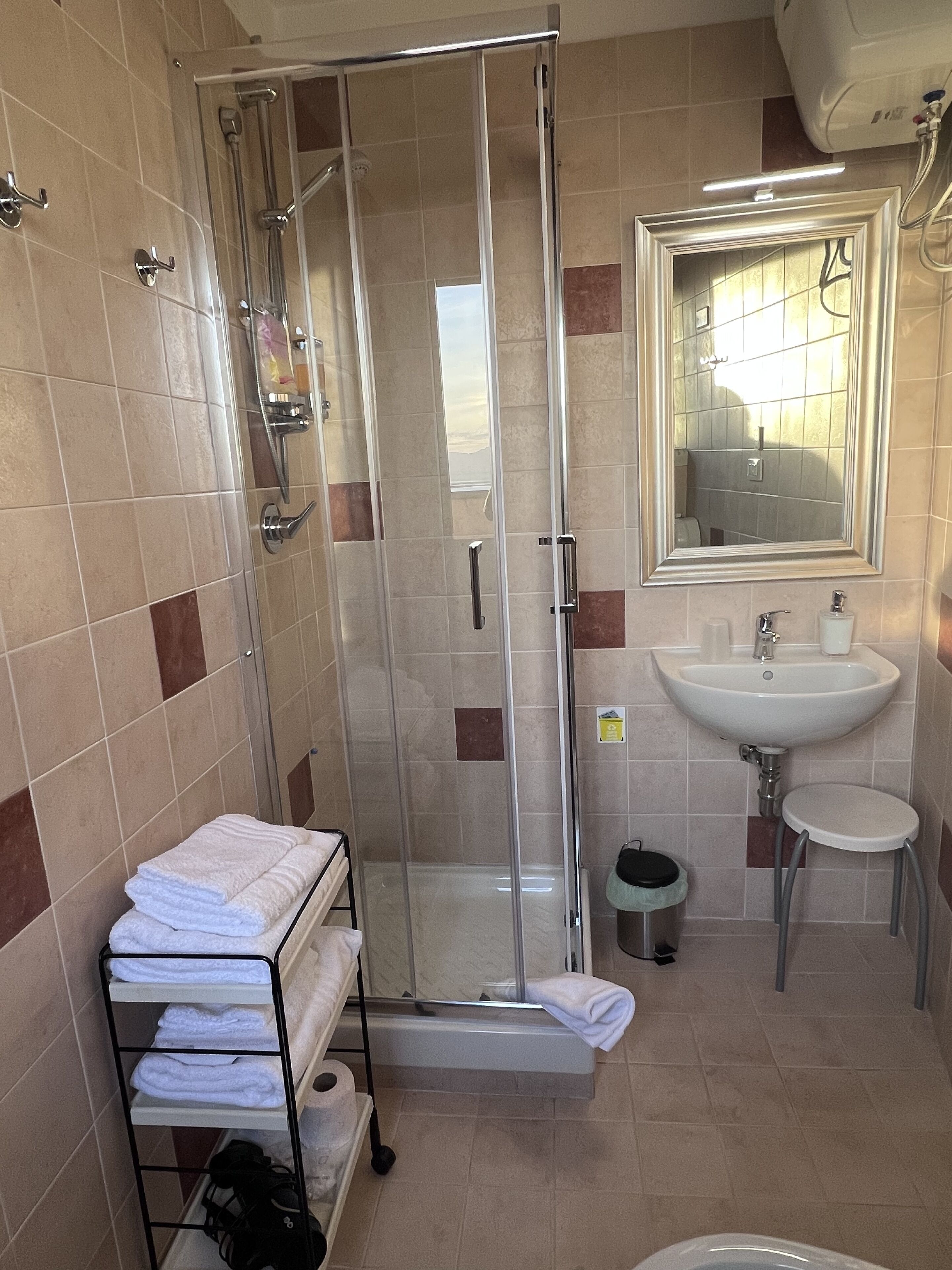 A bathroom with a glass shower enclosure, a sink, a mirror, and a towel rack with folded towels.