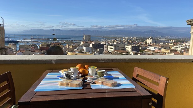 Een tafel met eten en drinken op een balkon met uitzicht op een stadsgezicht met gebouwen en een wateroppervlak.