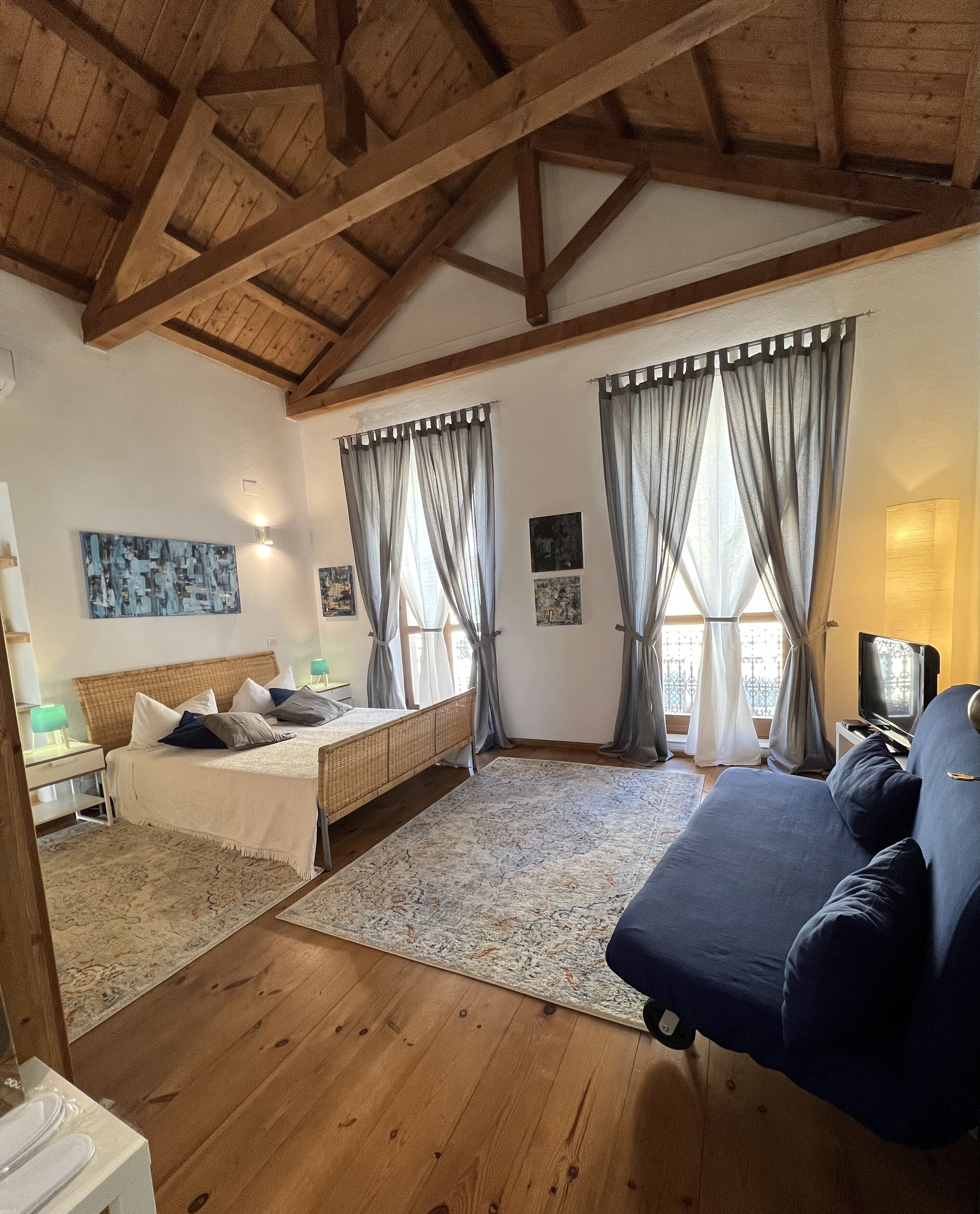 A room with a bed, a sofa, a TV, and artwork on the walls.