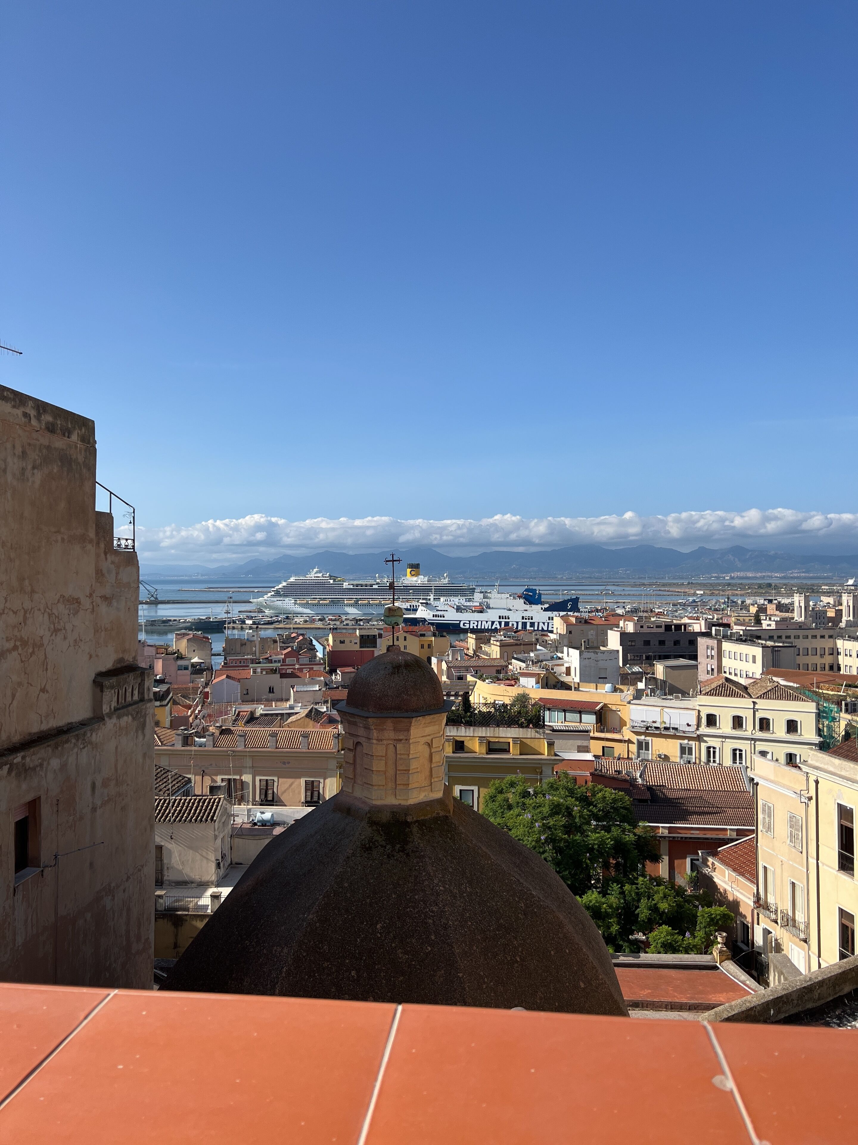 Un paisaje urbano con una cúpula destacada, un puerto con barcos y un cielo azul despejado.