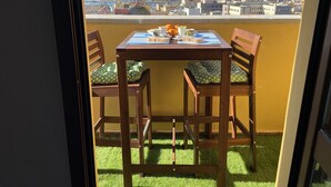 Een balkon met een tafel en stoelen, en een uitzicht op een stadsbeeld en bergen op de achtergrond.
