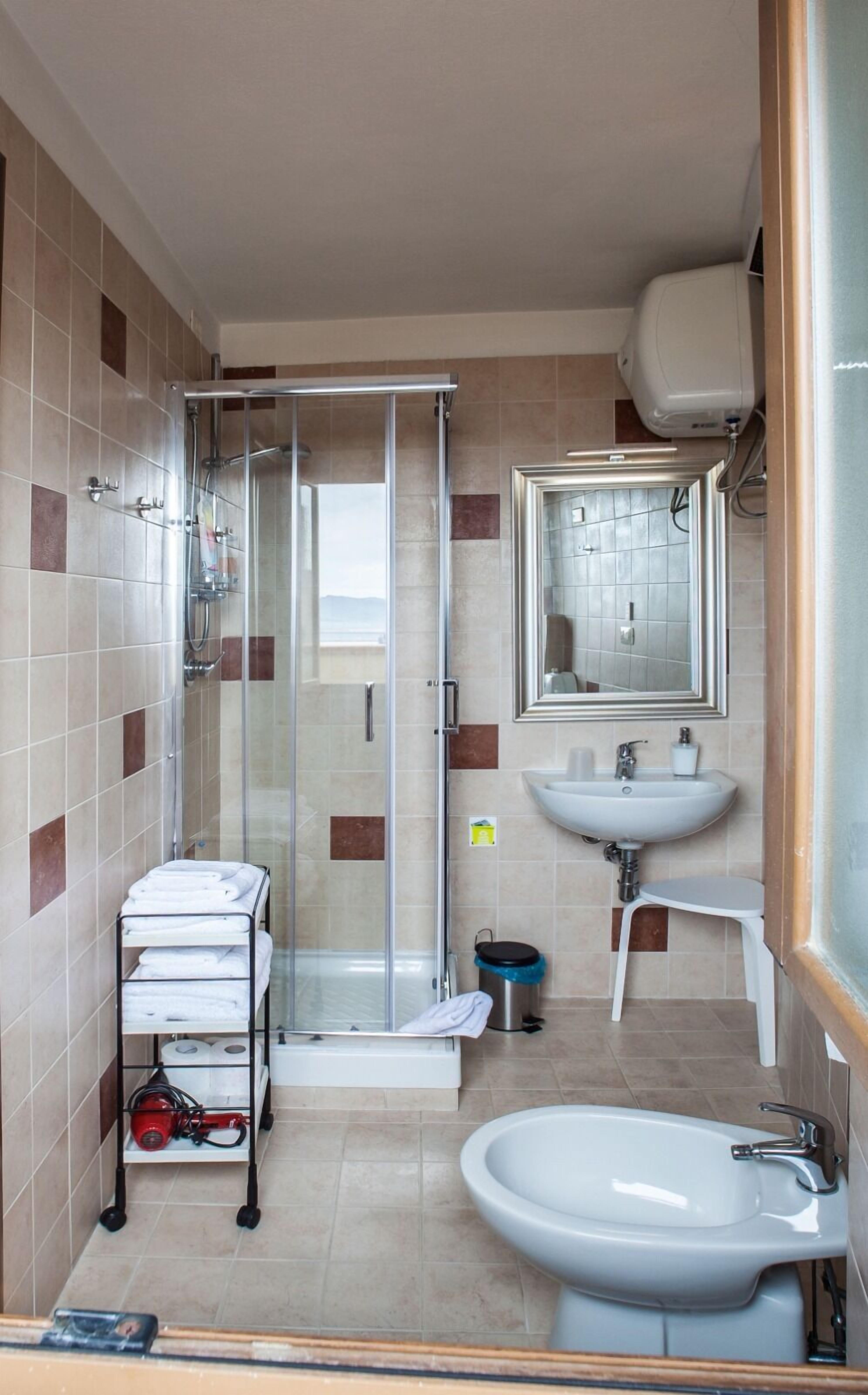 Een badkamer met een douche met glazen wand, een wastafel, een spiegel en een handdoekrek met handdoeken.