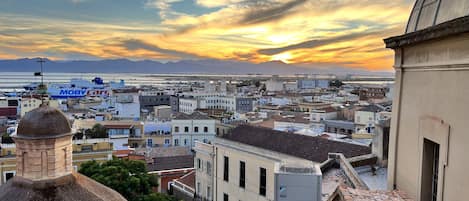 A cityscape with a sunset over the sea, featuring a mix of historical and modern architecture.