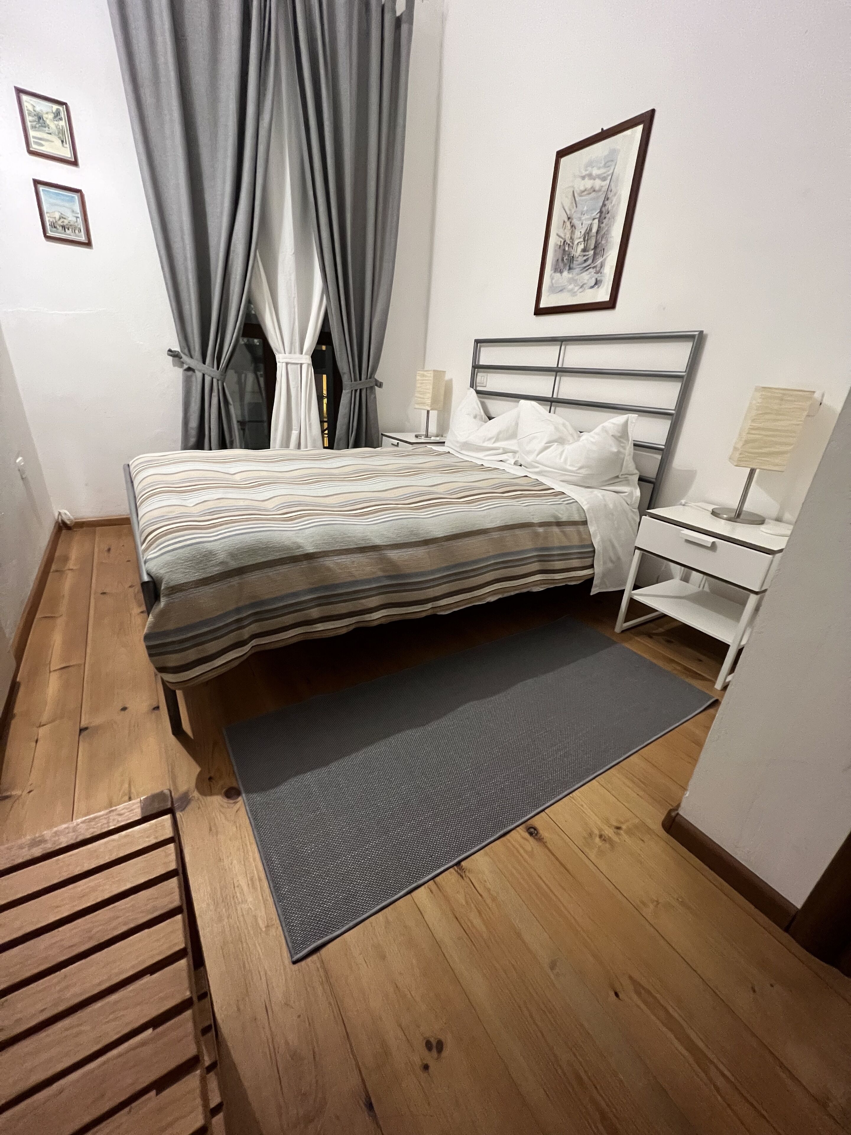 A neatly arranged bedroom with a bed, bedside tables, a nightstand, and a window with curtains.