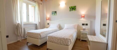A bedroom with two single beds, a nightstand with a lamp, a mirror, and a window with curtains.