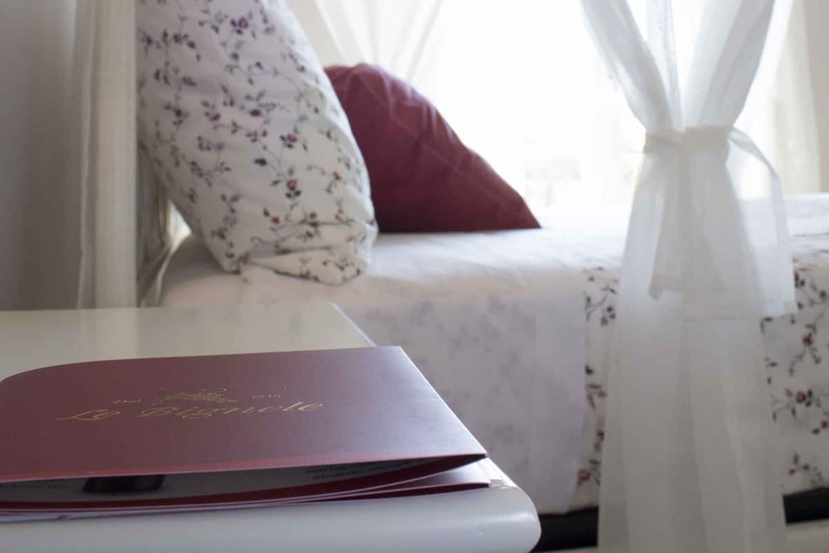Une chambre à coucher avec un lit à baldaquin, une table de chevet sur laquelle repose un livre rouge et un coussin à motifs floraux.