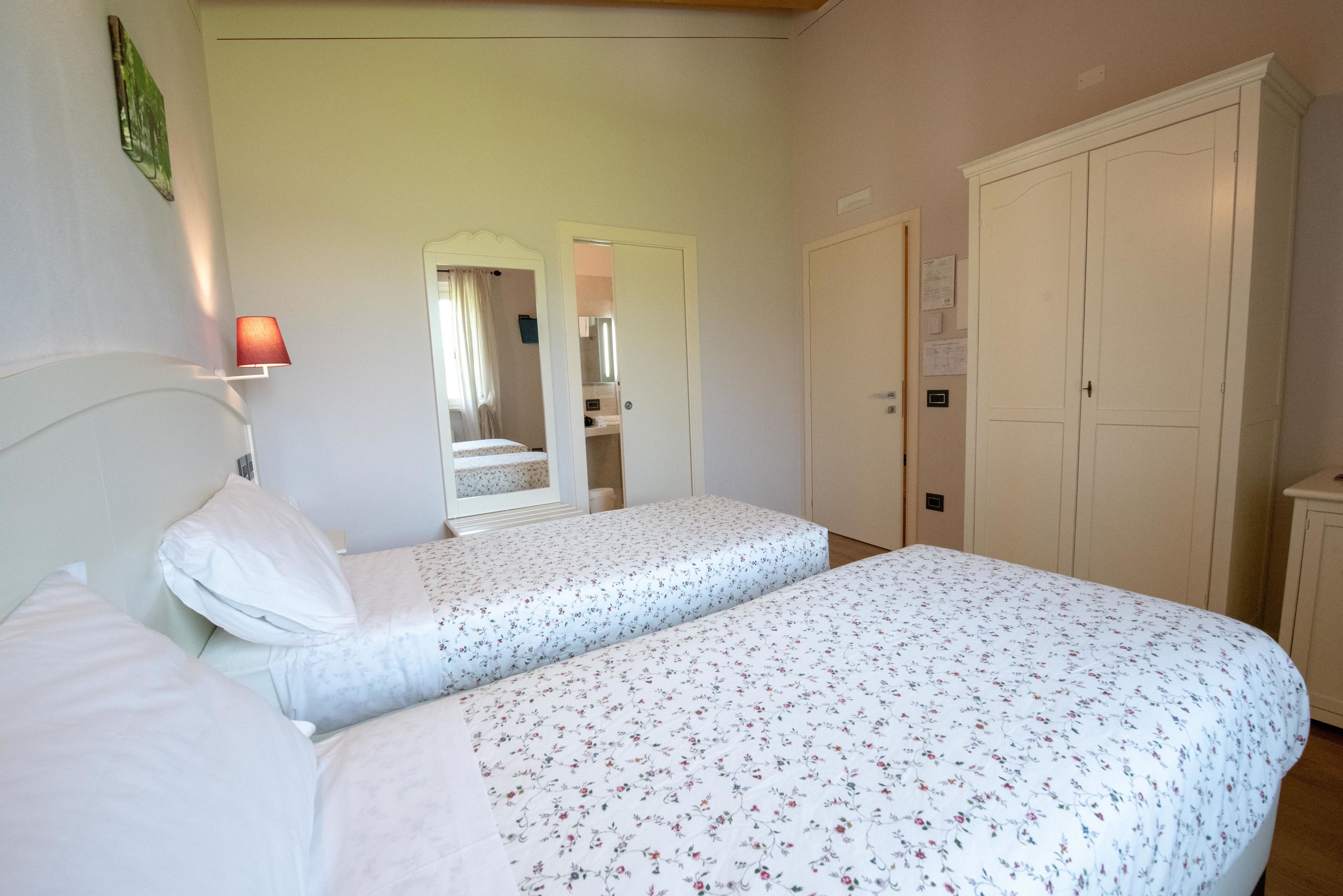 A bedroom with two single beds, a nightstand, a lamp, a wardrobe, and a mirror.