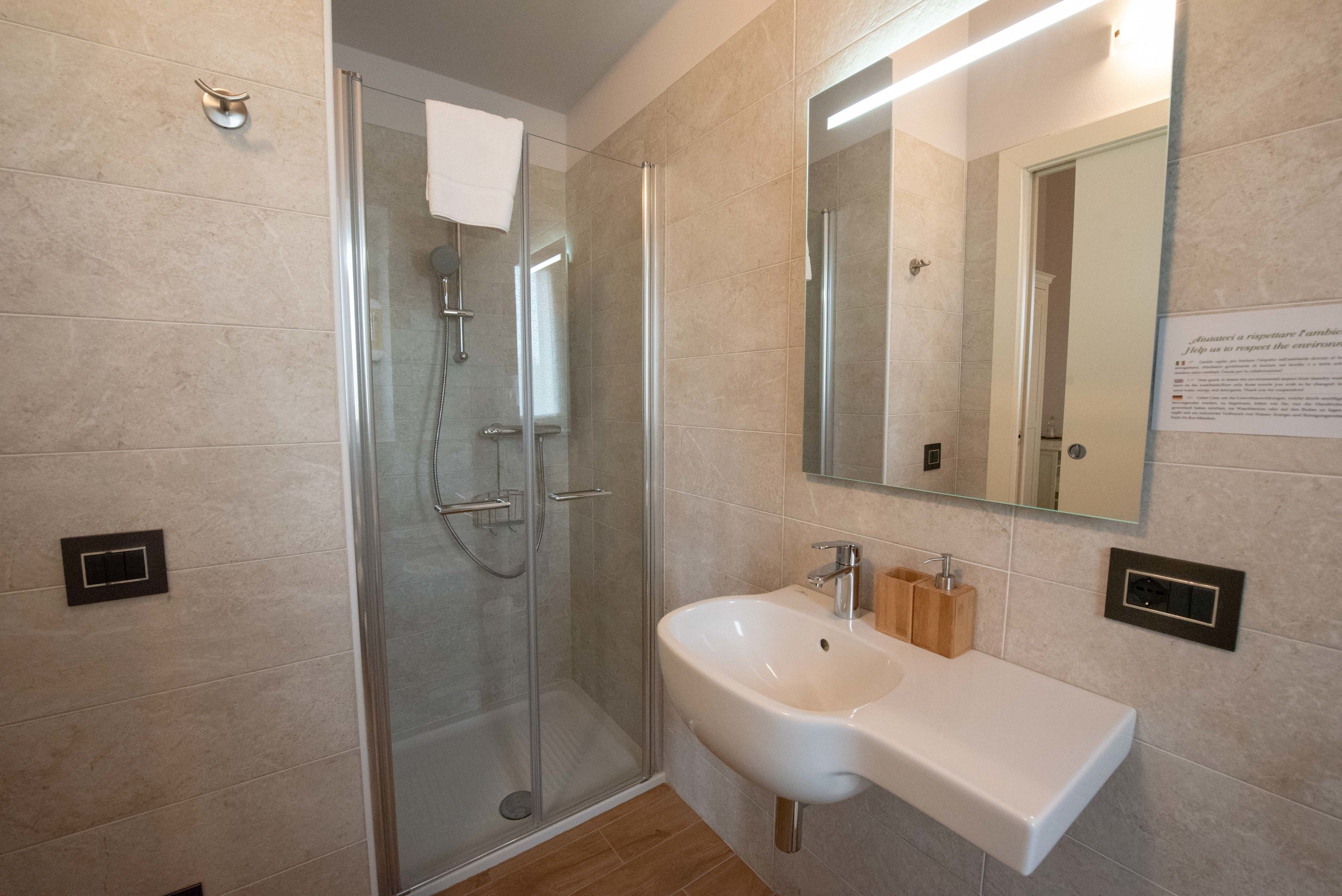 Un baño moderno con ducha acristalada, un lavabo blanco y un espejo encima.