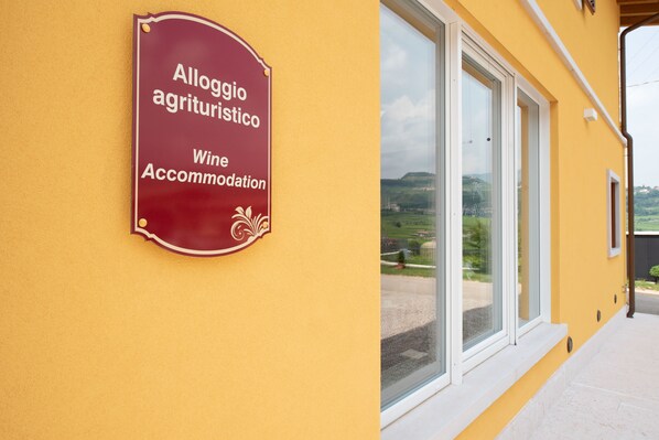 A sign for 'Alloggio agrituristico Wine Accommodation' on a yellow building.