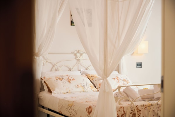 A bed with a canopy, floral bedding, and a bedside table with a lamp. - Le Bignele - Alloggio Agrituristico (Marano di Valpolicella)