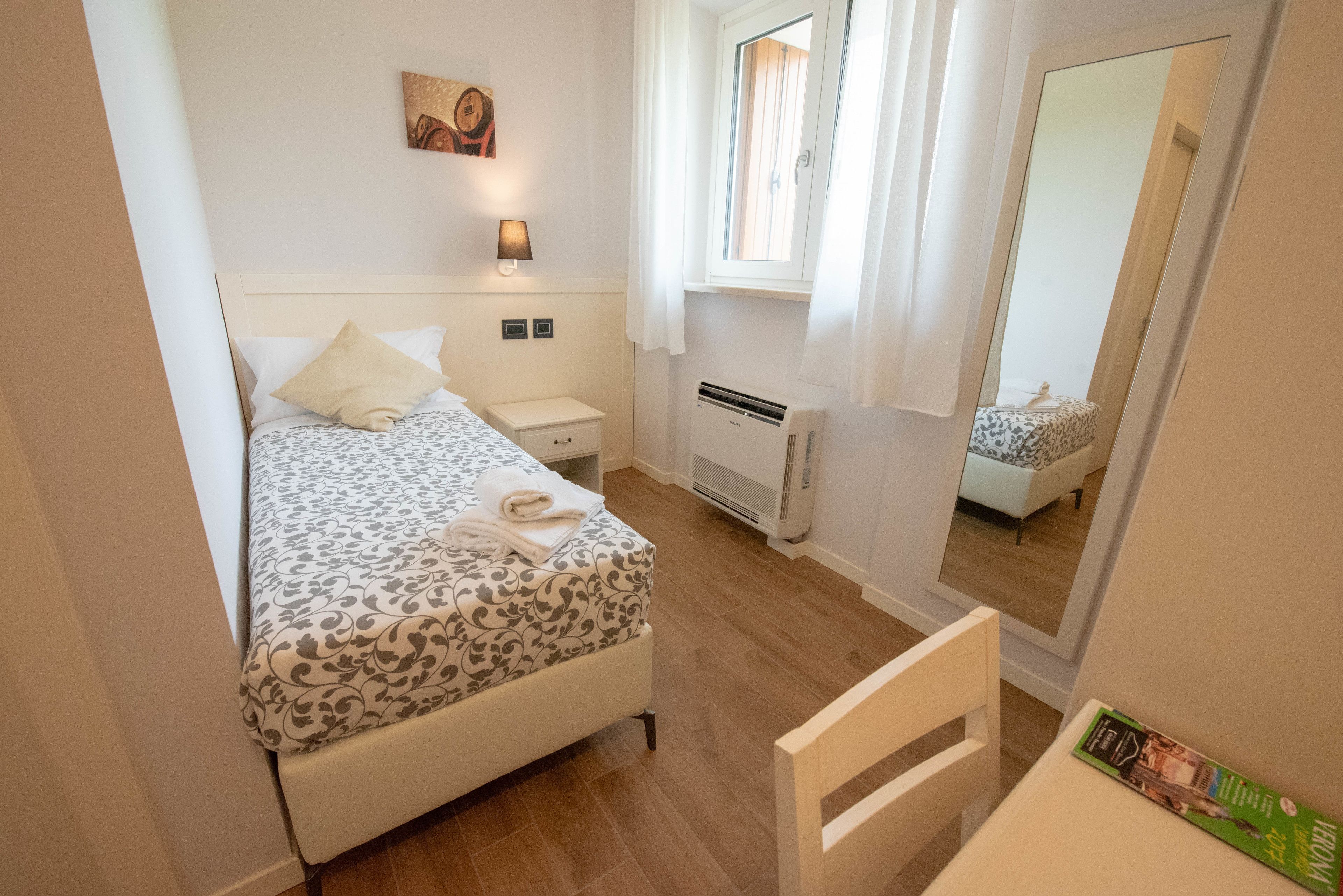 A bedroom with a bed, bedside table, lamp, air conditioning unit, and a mirror.