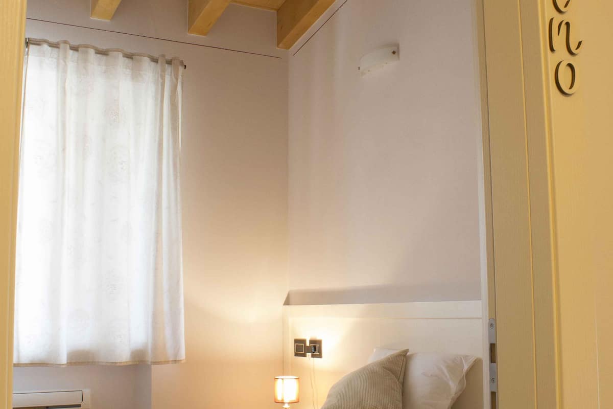 Une chambre d’hôtel avec un lit, une table de chevet, une lampe et une fenêtre avec des rideaux.