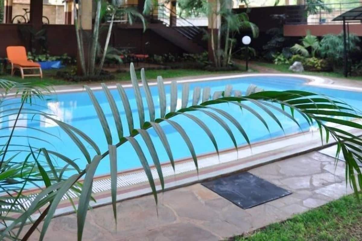 A multi-story building with balconies, a swimming pool, and palm trees.
